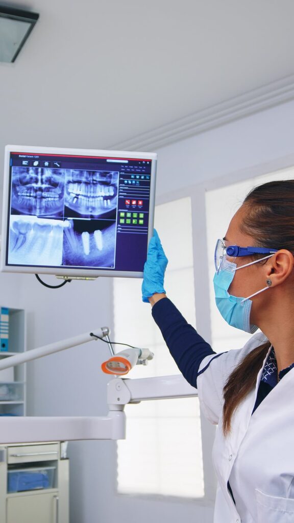 Digitale Röntgenaufnahmen am Monitor Karies erkennen im Röntgenbild: Zahnärztin mit Mundschutz und Schutzbrille prüft digitale Zahnaufnahmen am Monitor