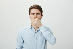Guy is gonna throw up. Worried shocked caucasian male model covering mouth with palm, looking nervous while trying to keep secret, standing against gray background. Man promised not to tell anything Mundgeruch-Behandlung beim Zahnarzt - Mann mit Halitosis