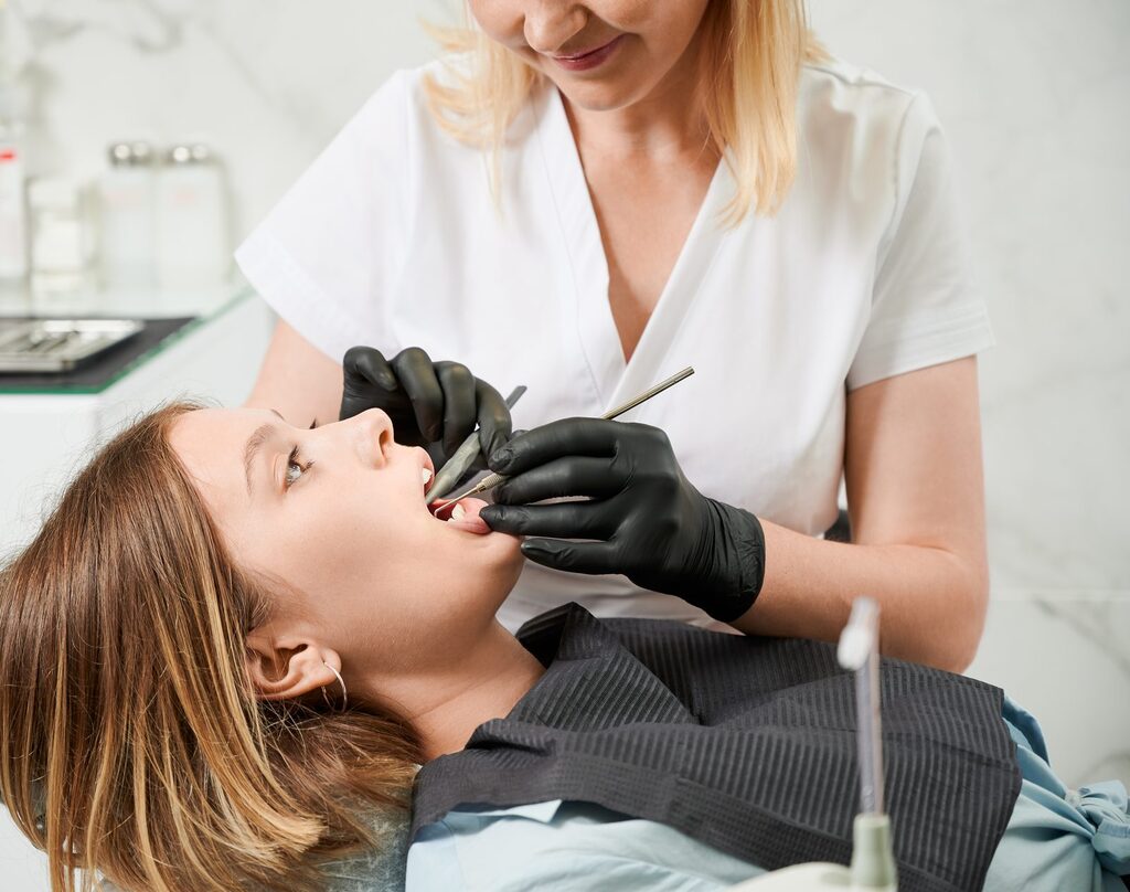 Kontrolltermin in der UPT-Nachsorge Zahnärztin untersucht mit Mundspiegel und Sonde die Zähne einer Patientin im Behandlungsstuhl beim Kontrolltermin