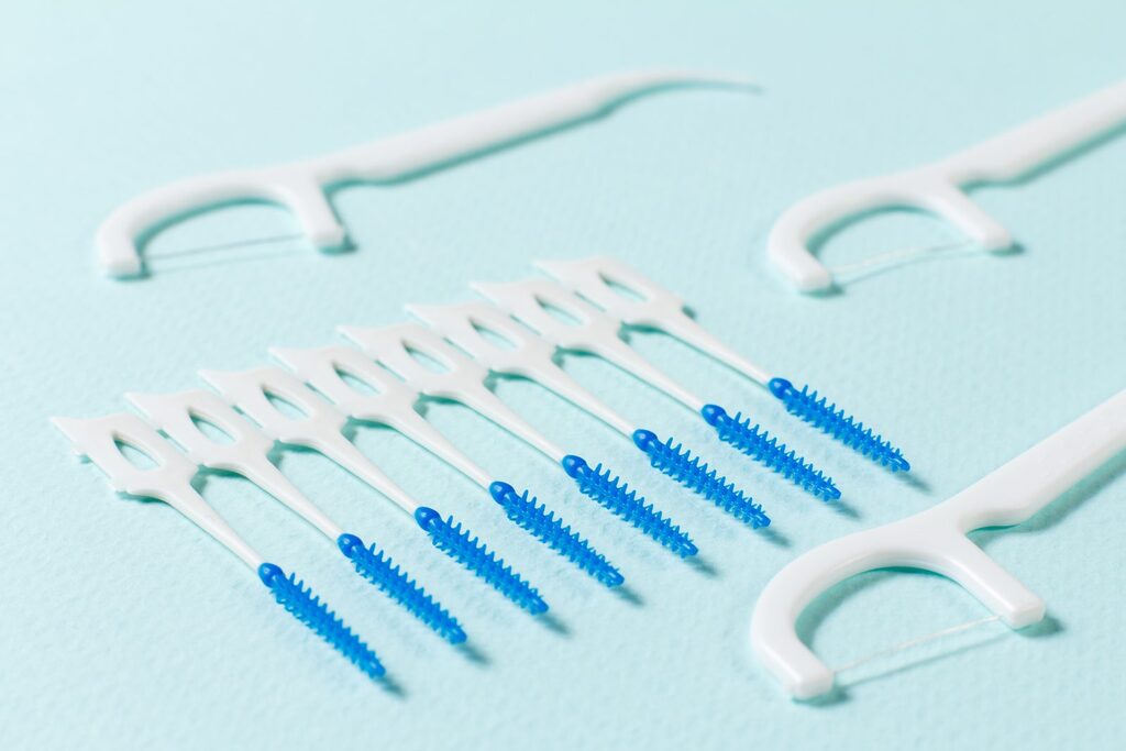 Hilfsmittel für die Zahnzwischenräume Zähne richtig putzen schließt die Zwischenräume ein: Interdentalbürsten und Zahnseide-Sticks auf hellblauem Untergrund